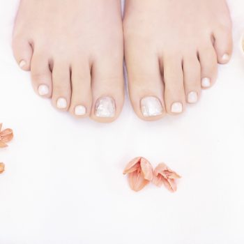 Female legs on a white background. Nails get a fresh and neat look during the pedicure procedure. Close up of female legs in spa salon.